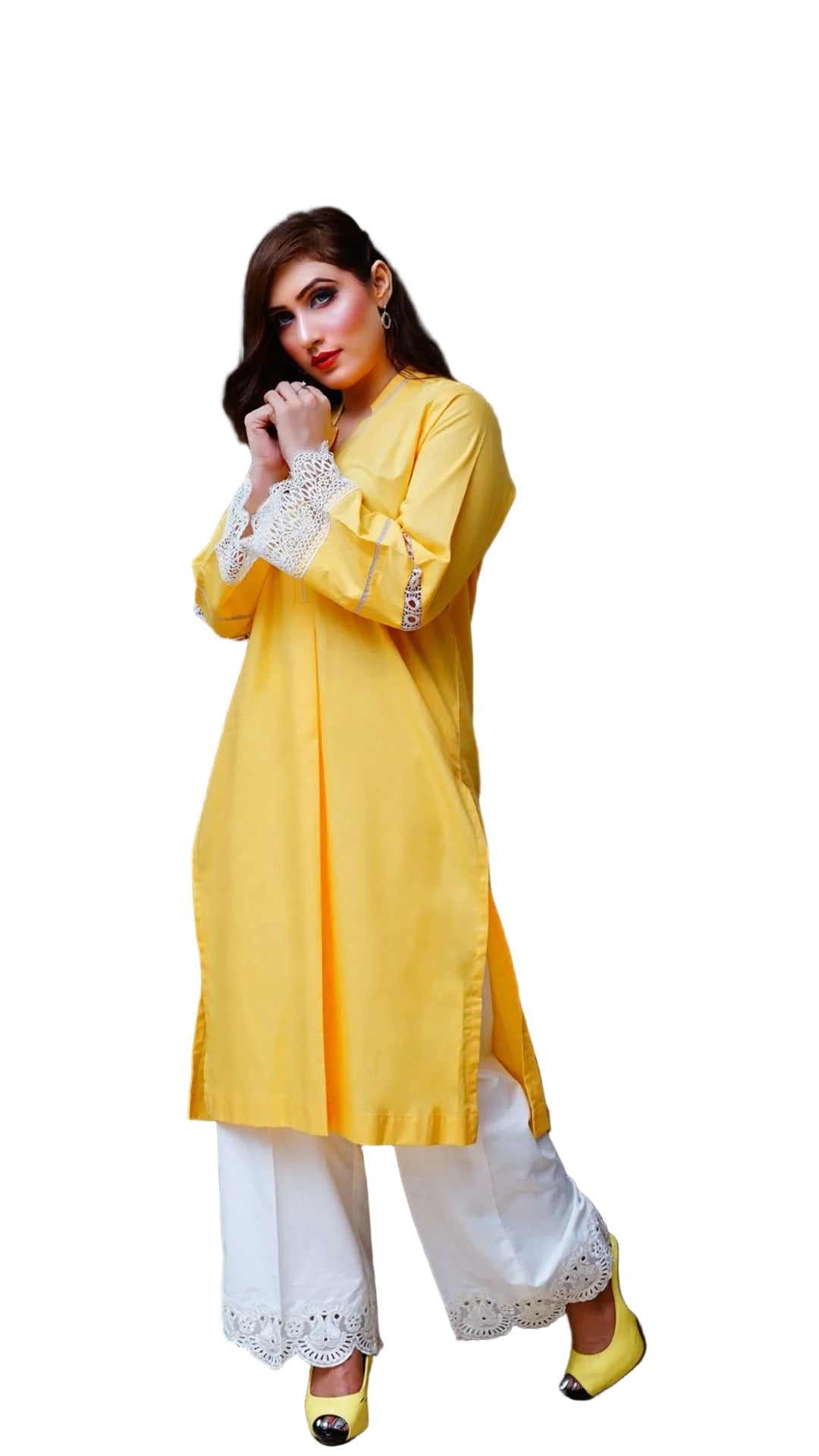 Woman in a yellow kurta with white lace details standing in a room with a gray chair and decorative plant.